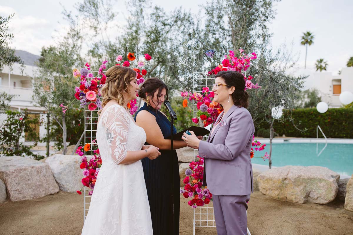 brides at wedding ceremony in lavender suit with hot pink flowers