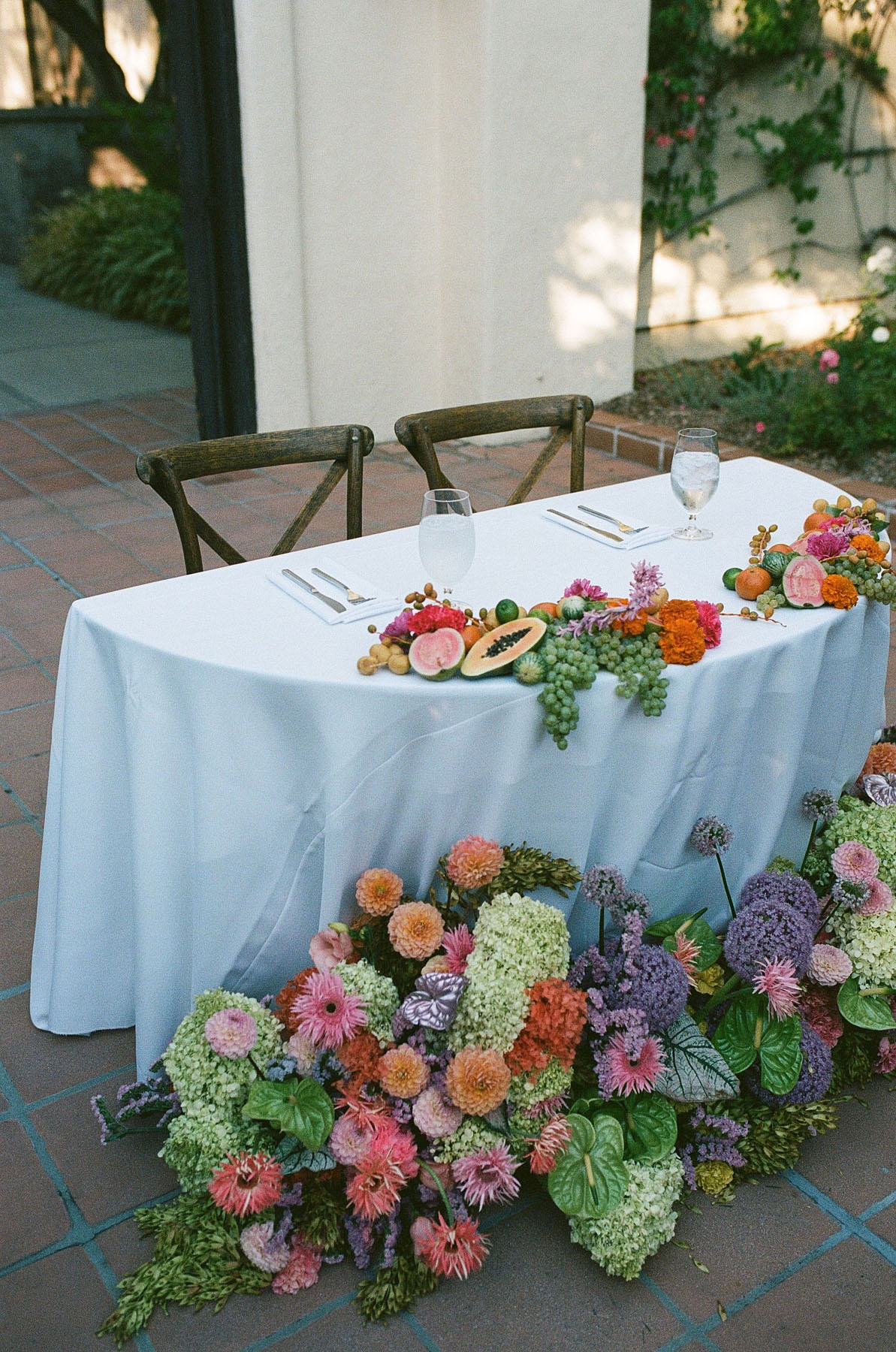 wedding sweetheart table with colorful green, orange, pink, and lavender florals and fruit