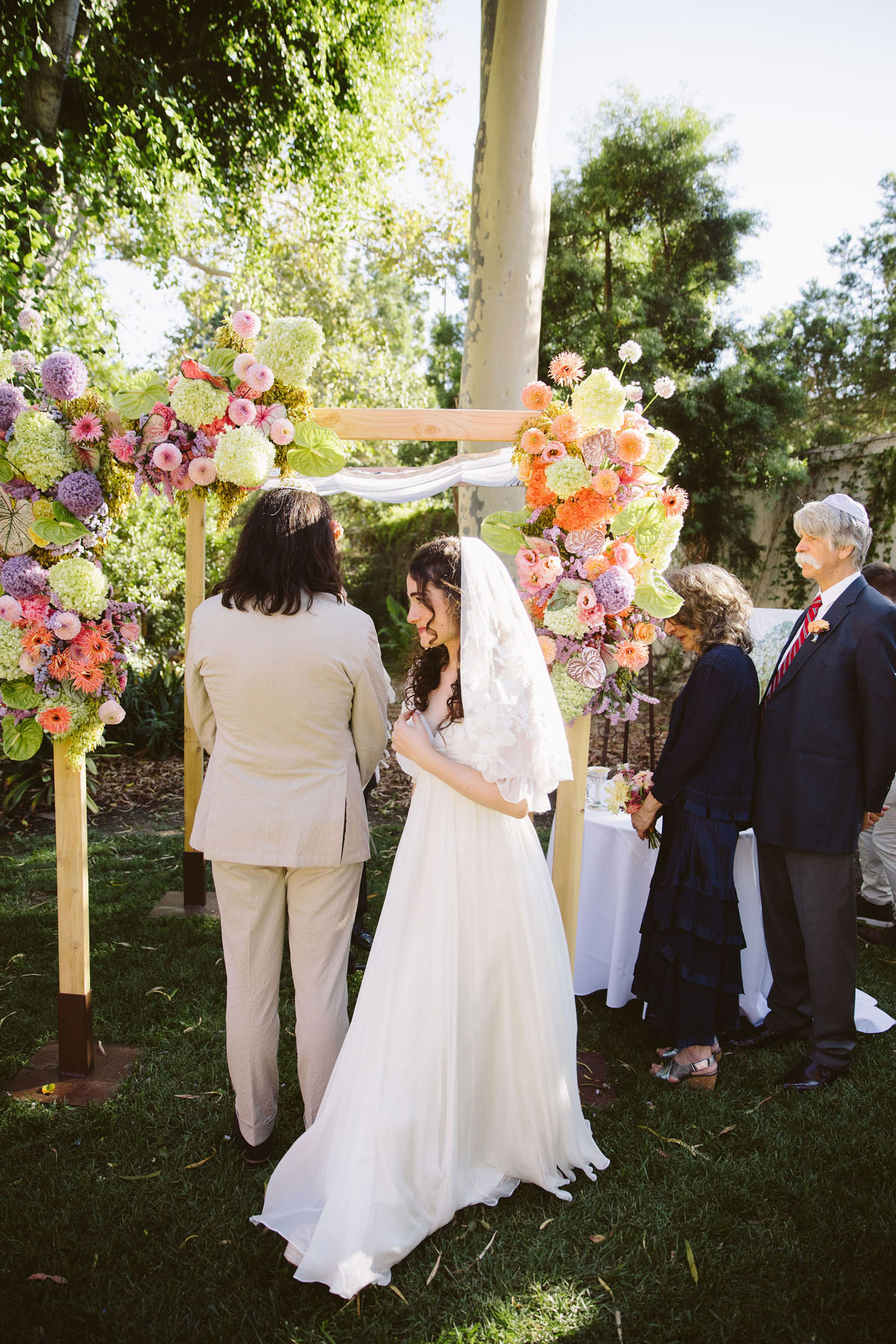 modern bedeken at jewish wedding ceremony in front of floral chuppah